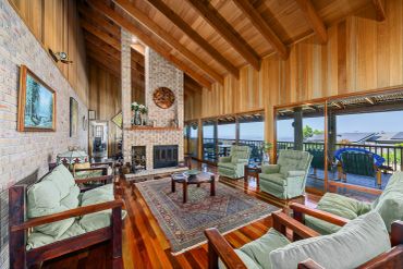 Cozy living room with wooden beams, brick fireplace, and large windows overlooking a balcony.