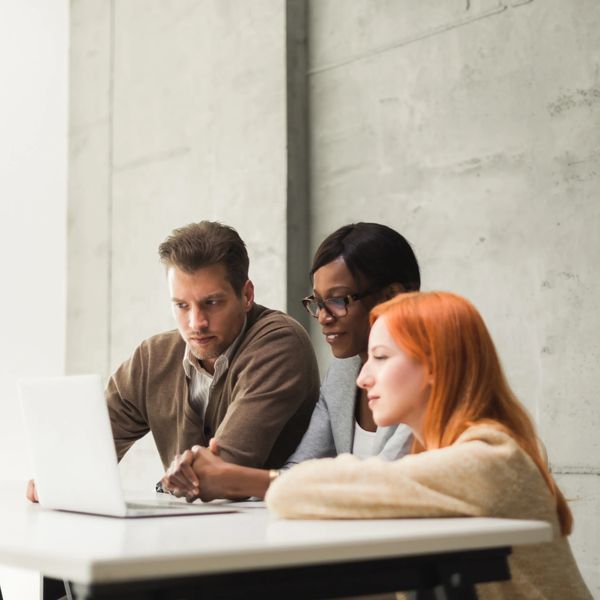 Three colleagues collaborating intensely over a laptop at a modern workspace.