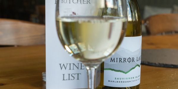 A glass of white wine with a bottle and menu on a wooden table.