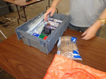 Person packing groceries into a gray plastic crate on a wooden table.