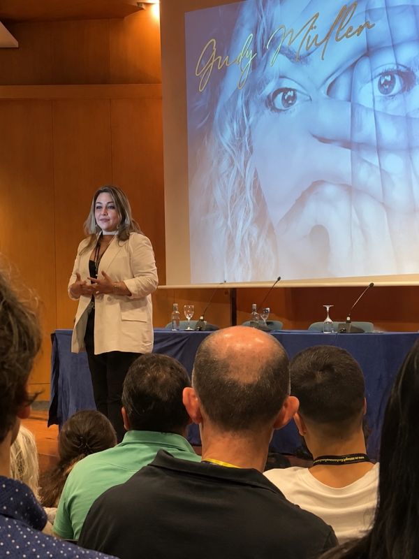 Woman giving a presentation in front of an audience with a large screen behind her.