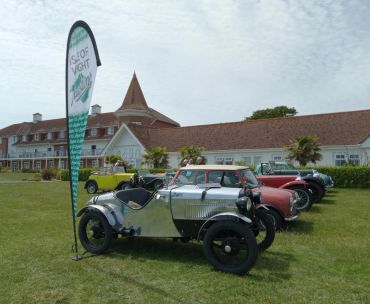 Classic vintage cars lined up on a lawn near a historic building.
