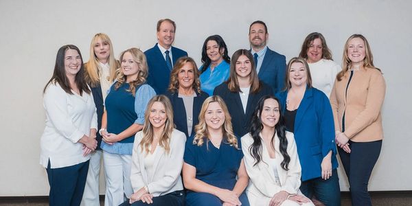 A professional group portrait of fourteen smiling colleagues in business attire.