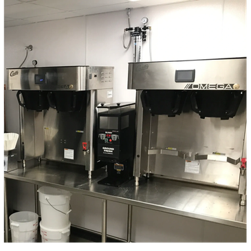 Two commercial coffee brewers on a stainless steel counter.