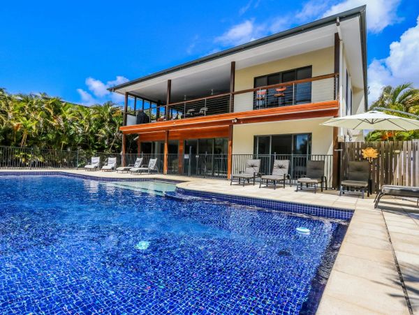 Modern two-story house with a blue tiled pool and lounge chairs.