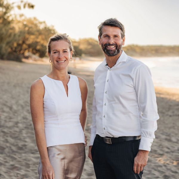 A smiling man and woman stand together on a beach at sunset.