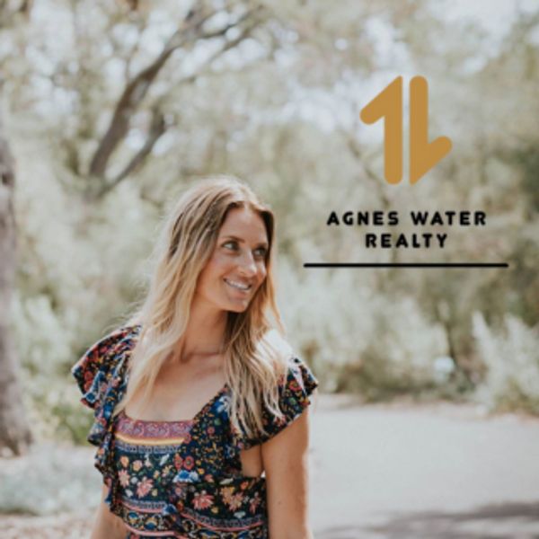 Smiling woman in floral dress with Agnes Water Realty logo outdoors.