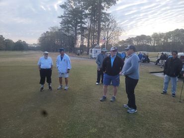 Group of people standing on a golf course in casual sportswear.