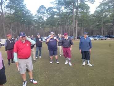 Group of older men standing on a golf course with clubs.