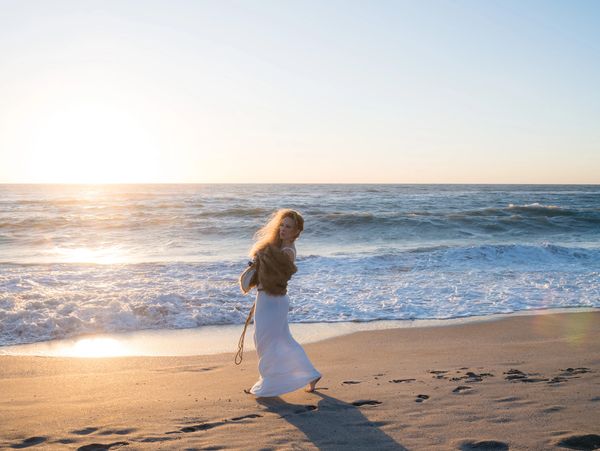 Woman walking on beach at sunset.