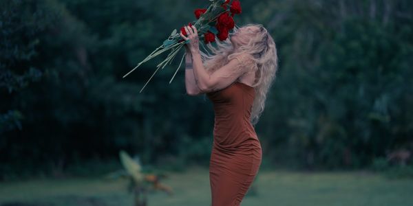 Woman in brown dress smelling red roses outdoors.