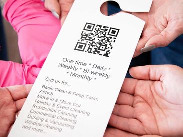 A hand holding a door hanger with cleaning service options and a QR code.
