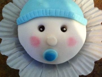 Cupcake decorated as a baby with a blue hat and pacifier.
