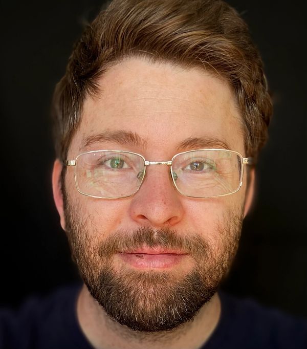 Close-up of a man with glasses and a beard against a dark background.