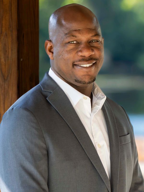 Smiling man in a gray suit and white shirt posing outdoors.