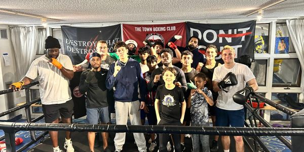 A diverse group of young boxers posing together in a boxing ring.