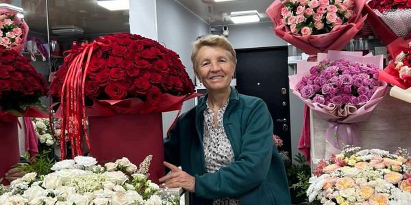 Smiling woman standing among large bouquets of roses in a flower shop.