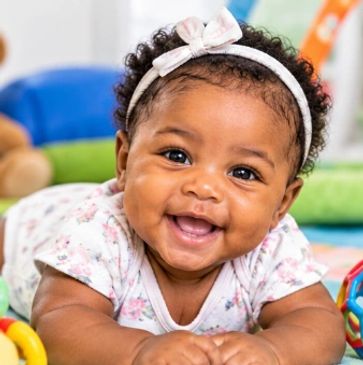 Smiling baby girl lying on her stomach, wearing a headband.