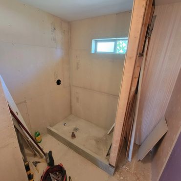 Unfinished shower area under construction with bare walls and small window.
