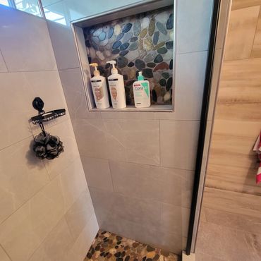 Shower niche with shampoo and body wash bottles against pebble tile background.