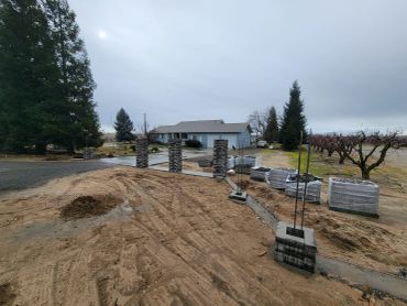 Construction site with stone pillars and building materials on dirt ground.