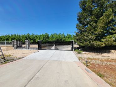 Modern driveway with a black metal gate and green trees under a clear blue sky.