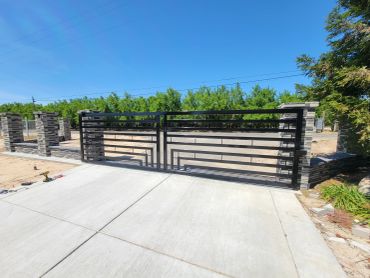 Modern black metal driveway gate with horizontal bars under a clear blue sky.