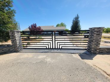 Modern black metal gate with stone pillars on a sunny day.