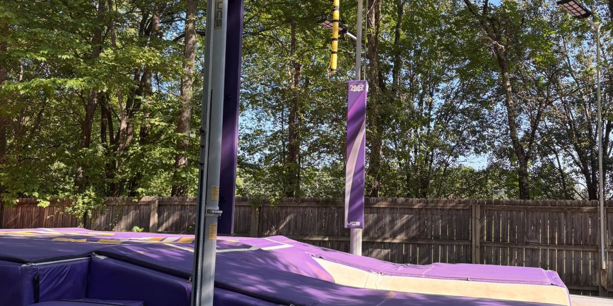 Purple trampoline setup outdoors with surrounding trees and fence.