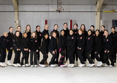 A group of female figure skaters posing on an ice rink in black outfits.