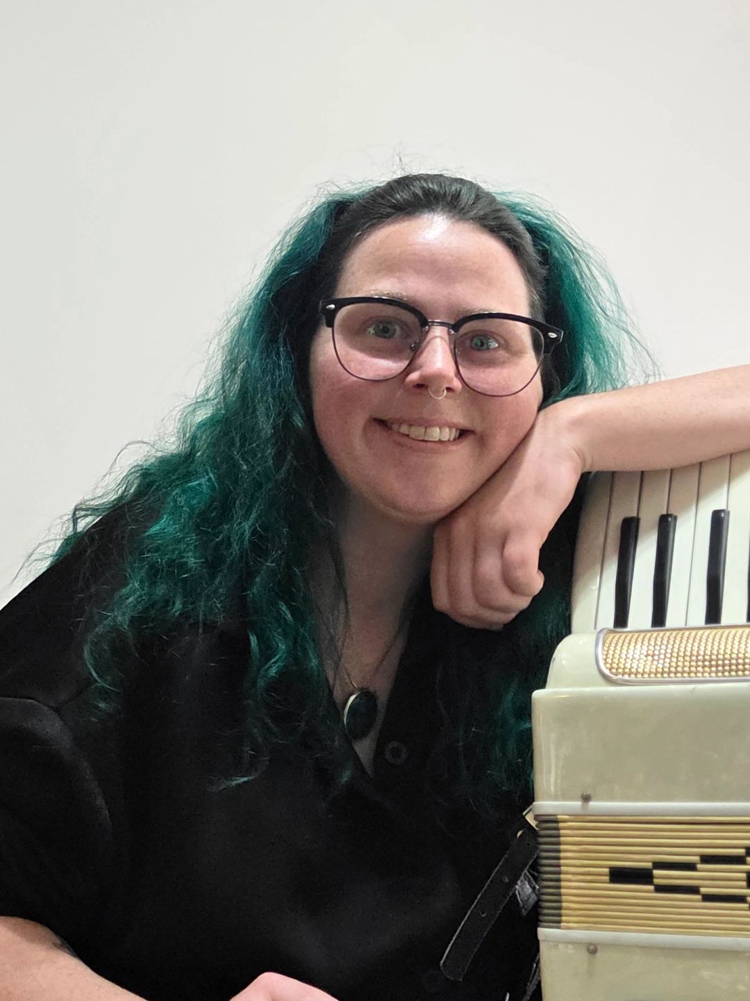 Person with glasses and teal hair smiling with an accordion.