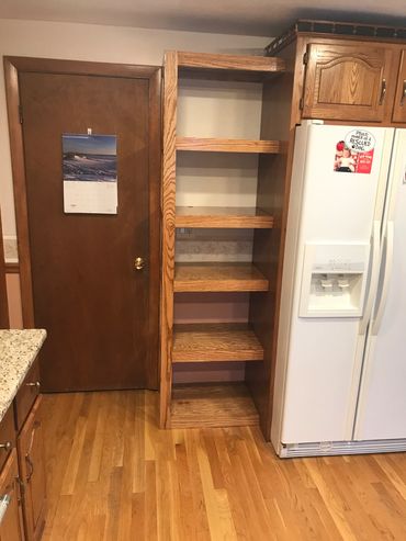 Empty wooden shelving unit between door and refrigerator.