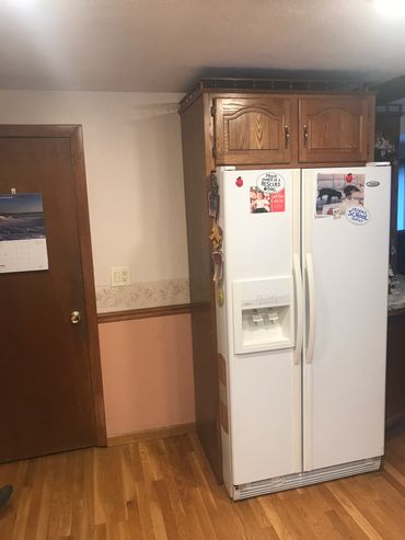 White side-by-side refrigerator with wooden cabinets above in kitchen corner.