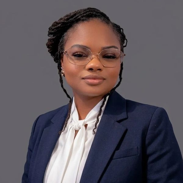 Confident woman in glasses and business attire against a gray background.