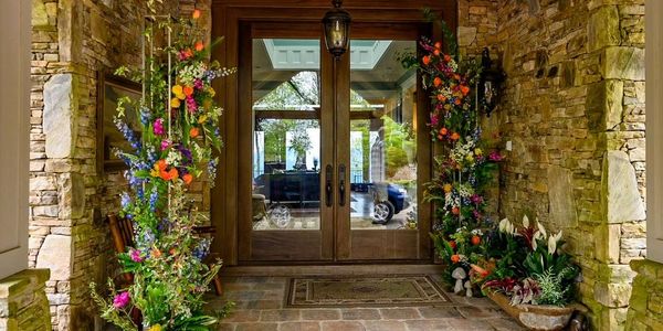 Ten foot tall wooden doors with glass flanked by nine foot tall columns of flowers surrounded by sto
