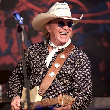 Smiling musician in cowboy hat playing guitar on stage.