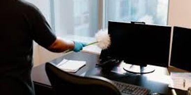 Person dusting computer screens in an office.
