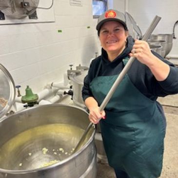 Mama Roo stirring a large or Mamas' Sauce in a kitchen.