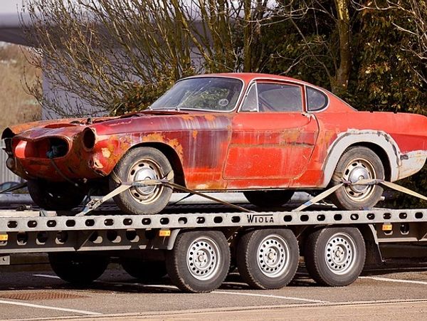 Rusty red vintage car on a flatbed trailer.