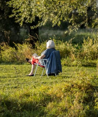 Elderly person sitting on a chair outdoors.