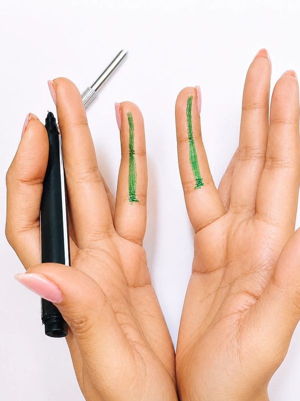 Hands with green lines drawn on two fingers using a marker held between fingers.