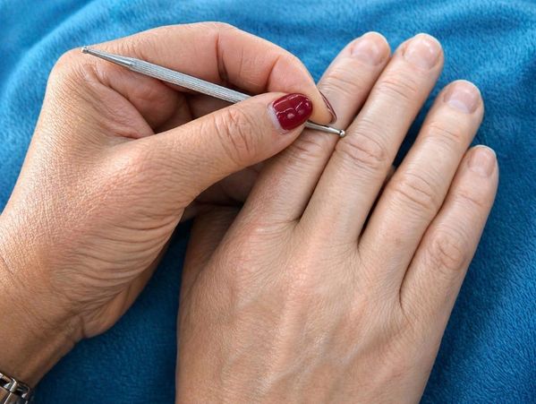 Hand using a metal tool to clean under fingernails on another hand.