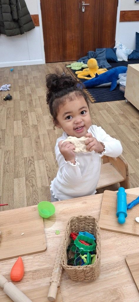 A young child playing with dough at a wooden table in a cozy room.