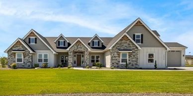 Front exterior of craftman-style luxury home with earth tone stone popouts and roof with steep peaks