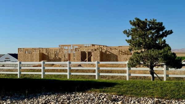 Wood framing of a luxury custom home being built with white fence and tree in front