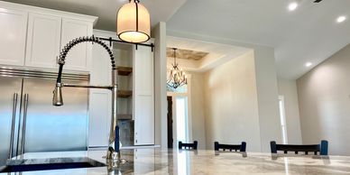 Farmhouse faucet granite counter white custom cabinets with a view of chandelier.