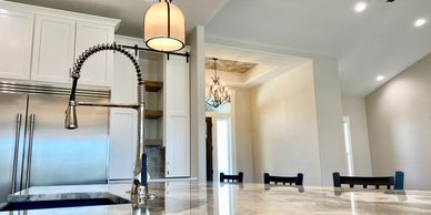 Farmhouse faucet granite counter white custom cabinets with a view of chandelier.