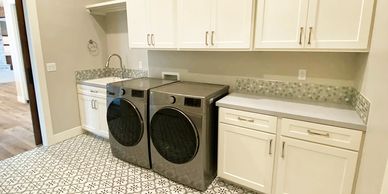 Laundry room with decorative tile and penny rounds backsplash with custom white cabinets.