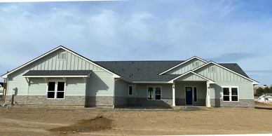 Front view of a home with light sage green siding and lower brown stonework.