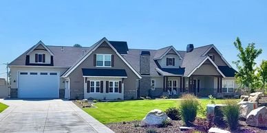 Street view of home with brown roof, stonework and dark wood eves and pillars with dark shutters.